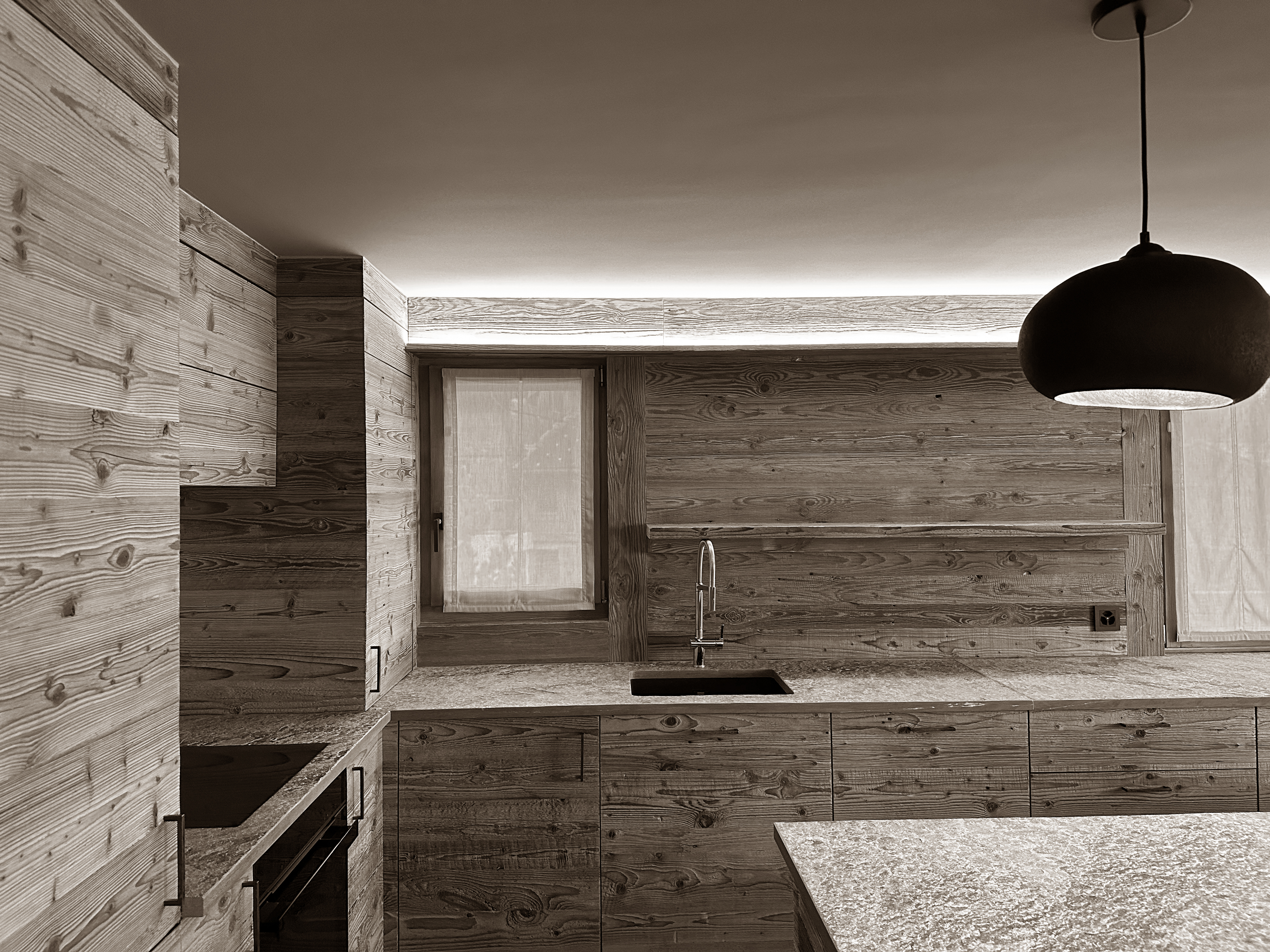 Beautifully crafted kitchen enveloped in natural wood, with seamless cabinetry and textured stone countertops. A sculptural pendant light and soft, recessed illumination highlight the warm, alpine character of the space while offering a modern and functional layout.