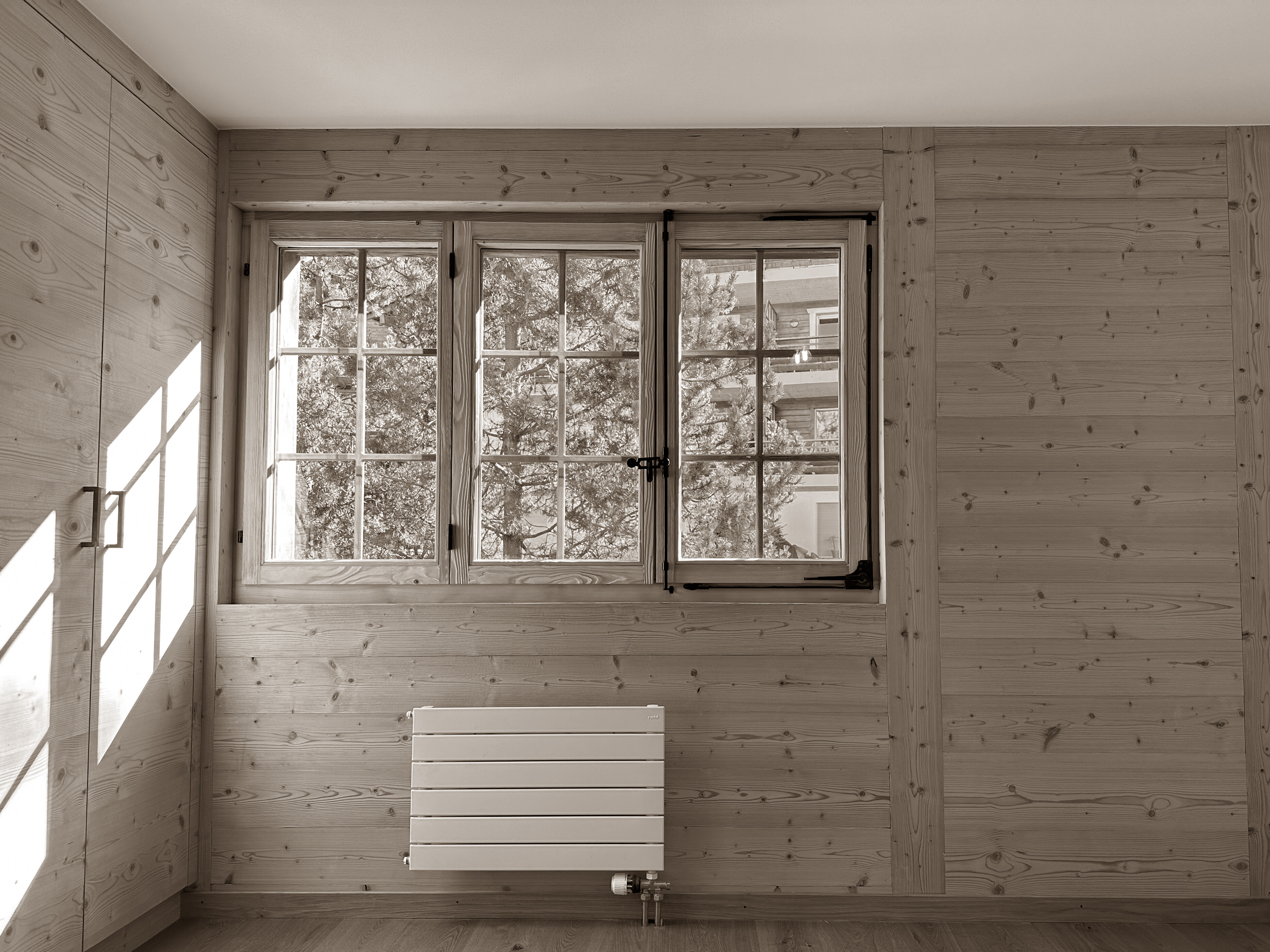 Bright and cozy room adorned with natural wood paneling, featuring a traditional window that frames views of the surrounding trees, filling the space with soft daylight and a warm alpine charm.