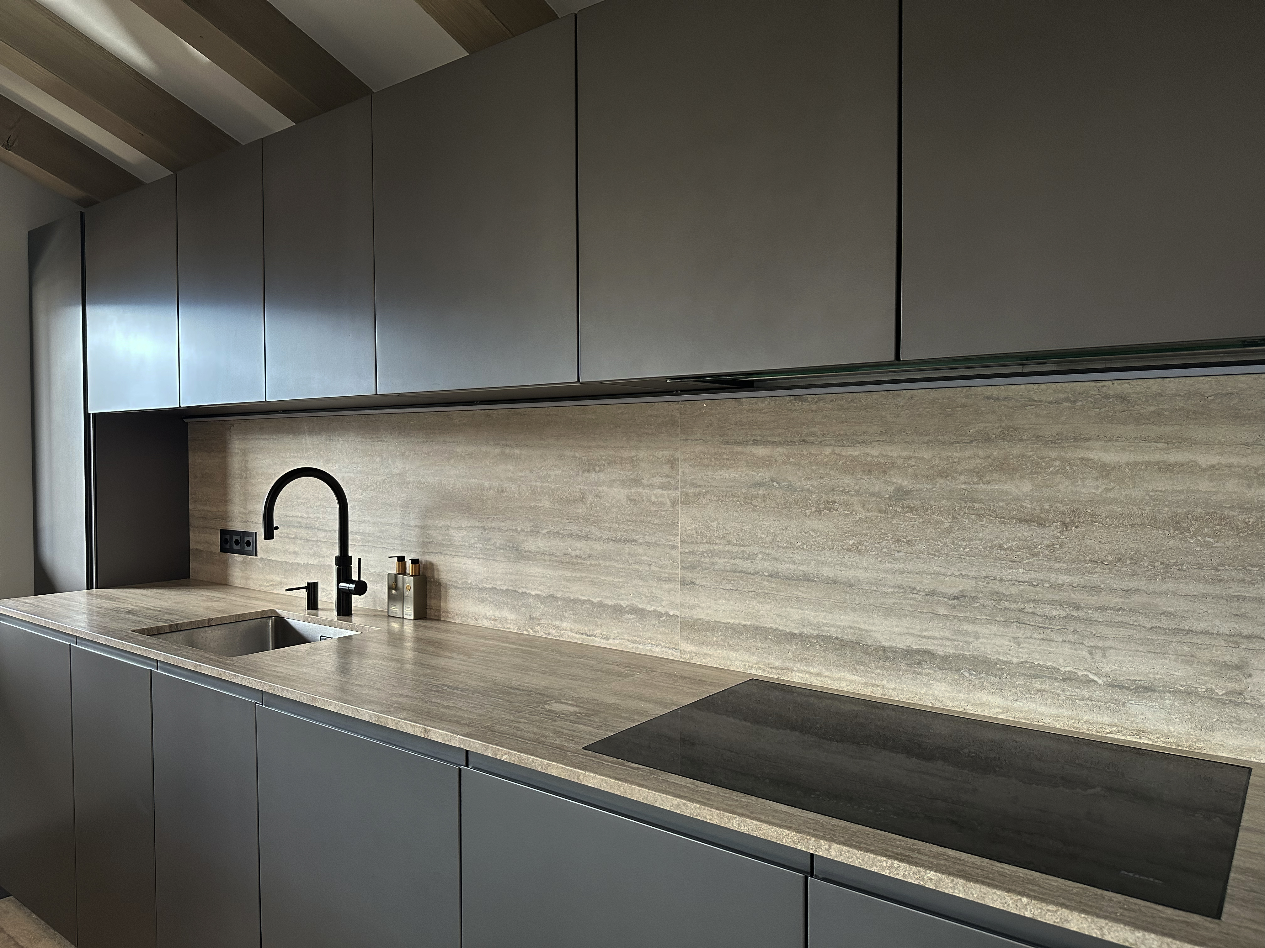 Minimalist kitchen design featuring matte cabinetry, a seamless natural stone backsplash, and elegant black fixtures. The refined textures and clean lines create a sophisticated yet functional workspace, perfectly integrated into the chalet’s modern alpine aesthetic. Minimalist kitchen design featuring matte cabinetry, a seamless natural stone backsplash, and elegant black fixtures. The refined textures and clean lines create a sophisticated yet functional workspace, perfectly integrated into the chalet’s modern alpine aesthetic.