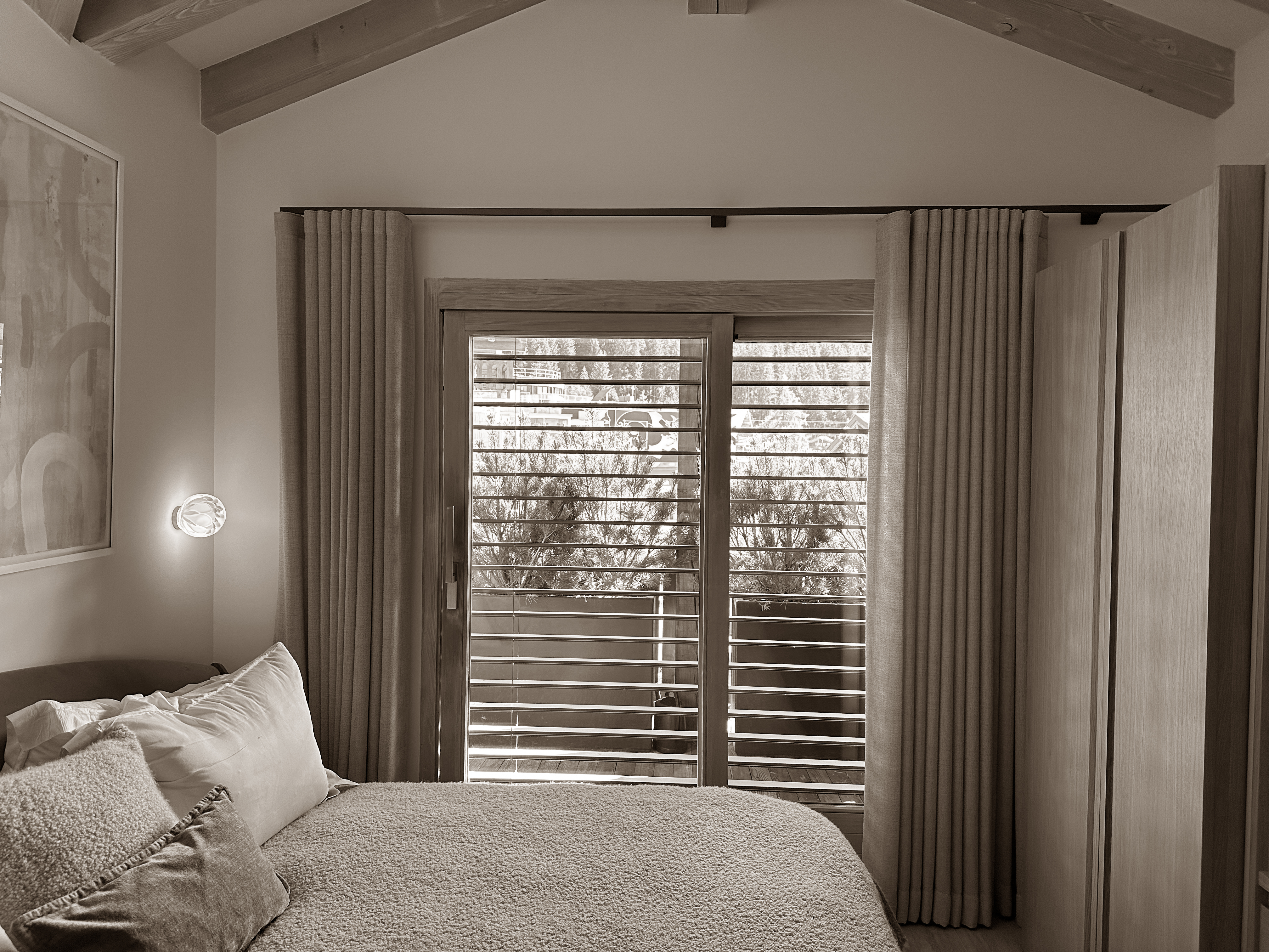 Serene bedroom retreat with soft, layered textures and natural materials, featuring with curtains and a private balcony framed by wooden shutters. The vaulted ceiling and warm lighting create a peaceful ambiance ideal for restful moments. Serene bedroom retreat with soft, layered textures and natural materials, featuring with curtains and a private balcony framed by wooden shutters. The vaulted ceiling and warm lighting create a peaceful ambiance ideal for restful moments.