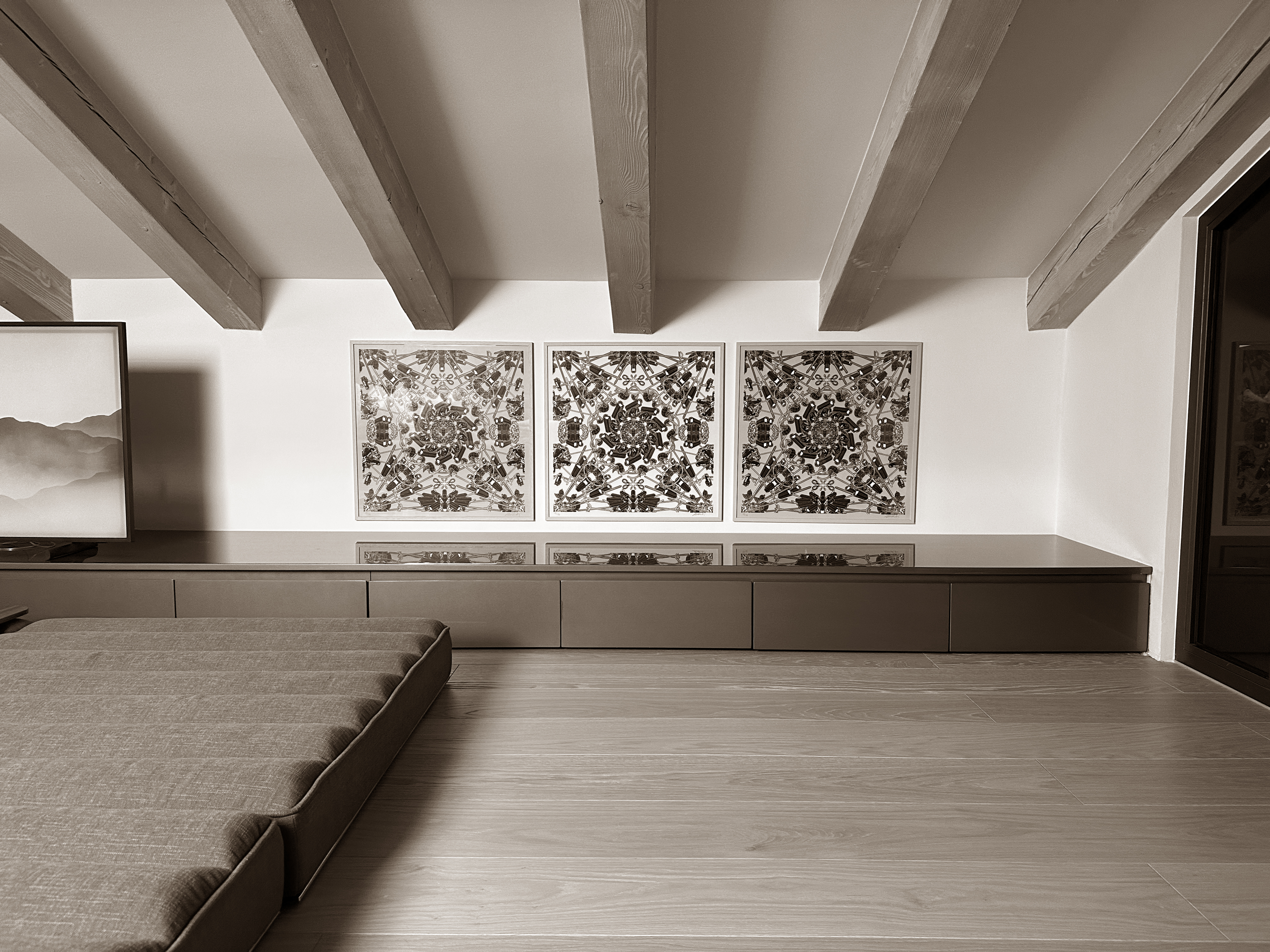 Contemporary lounge area tucked beneath exposed wooden beams, featuring a low, built-in media console and bold, symmetrical artwork that brings visual interest to the space. Contemporary lounge area tucked beneath exposed wooden beams, featuring a low, built-in media console and bold, symmetrical artwork that brings visual interest to the space.