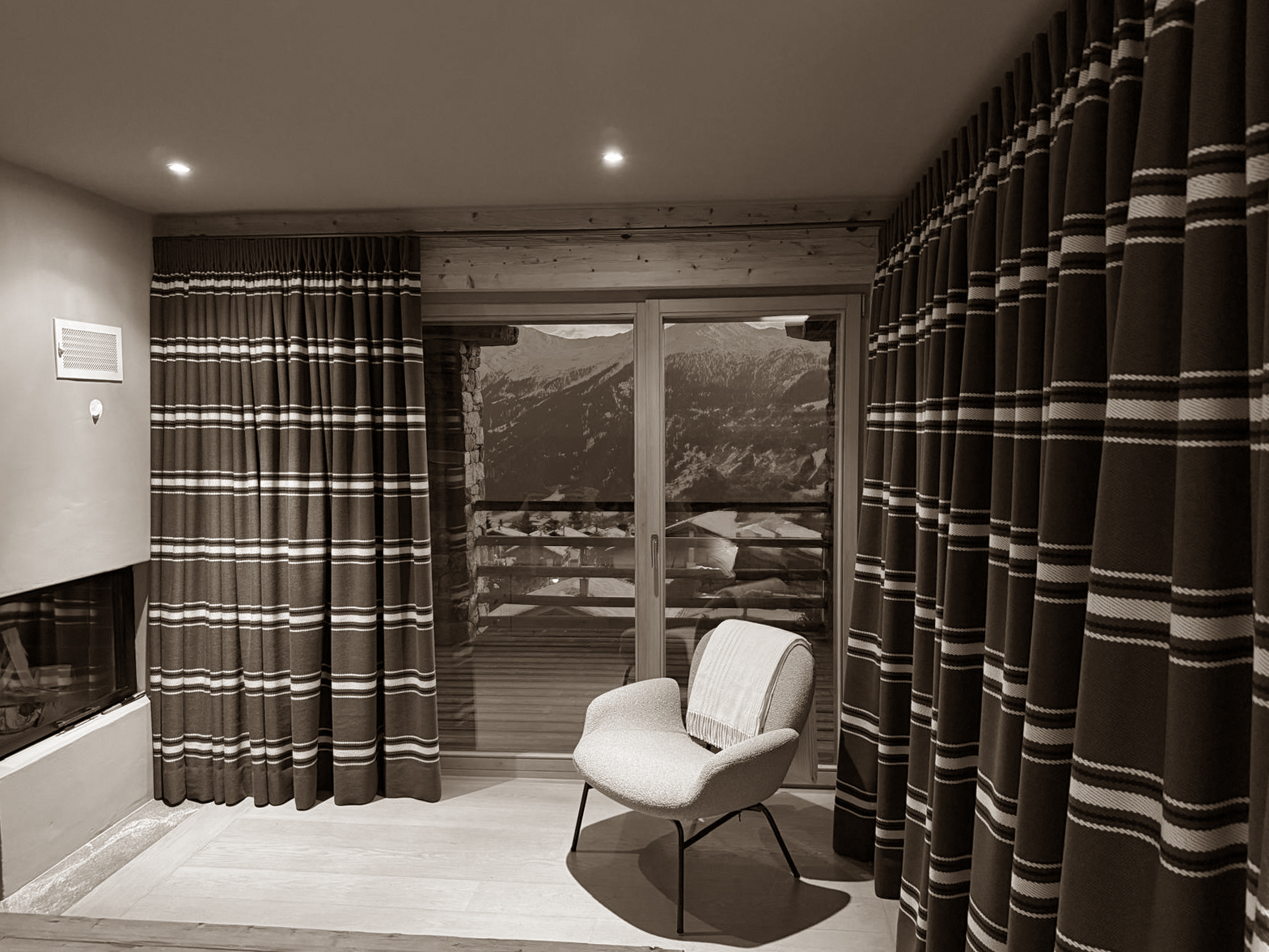 A serene reading spot with alpine views, framed by bold striped curtains and warmed by a nearby fireplace.