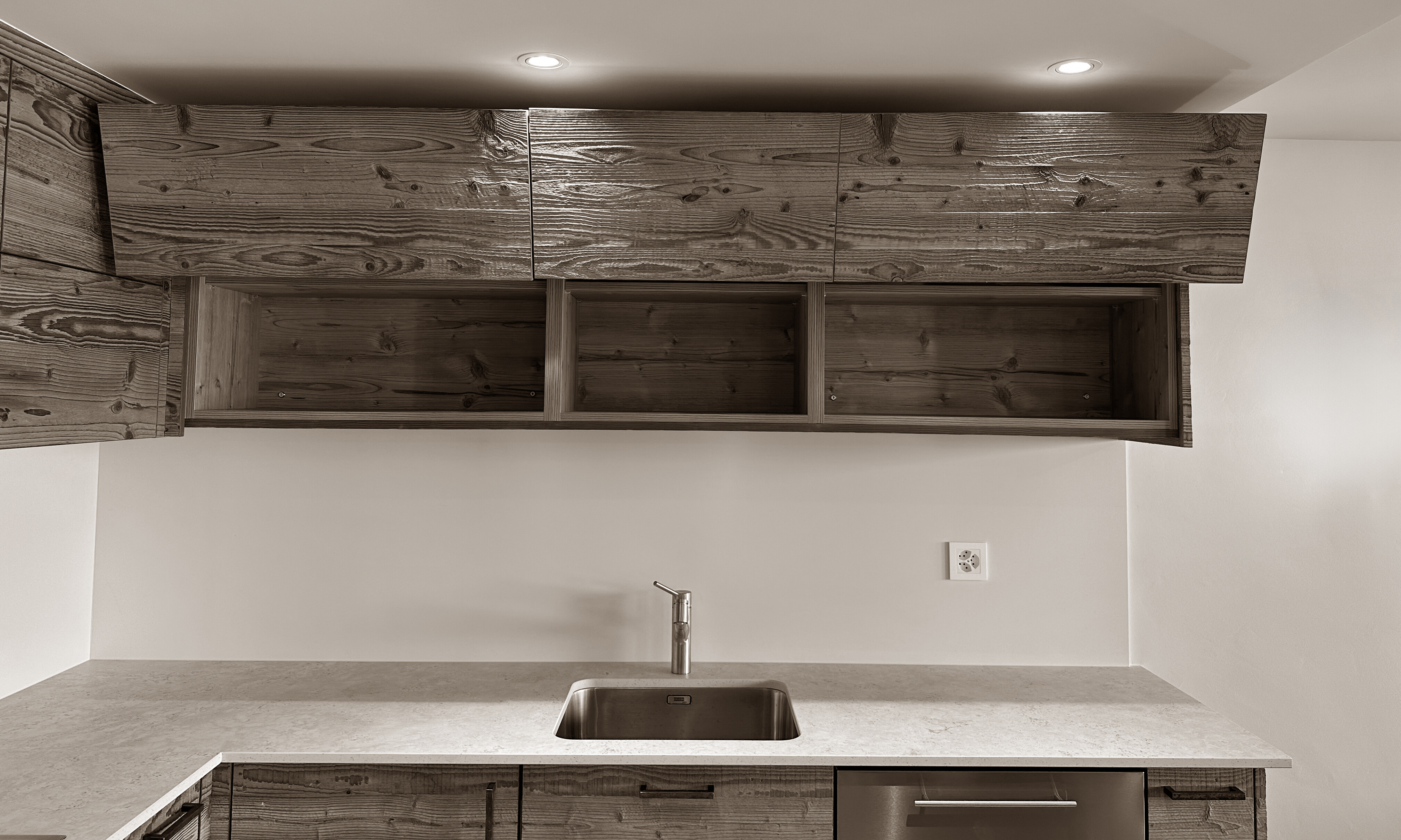Modern kitchen detail featuring sleek wooden cabinetry with upward-opening doors, a minimalist sink, and a smooth stone countertop, all enhanced by subtle recessed lighting for a clean and sophisticated look.