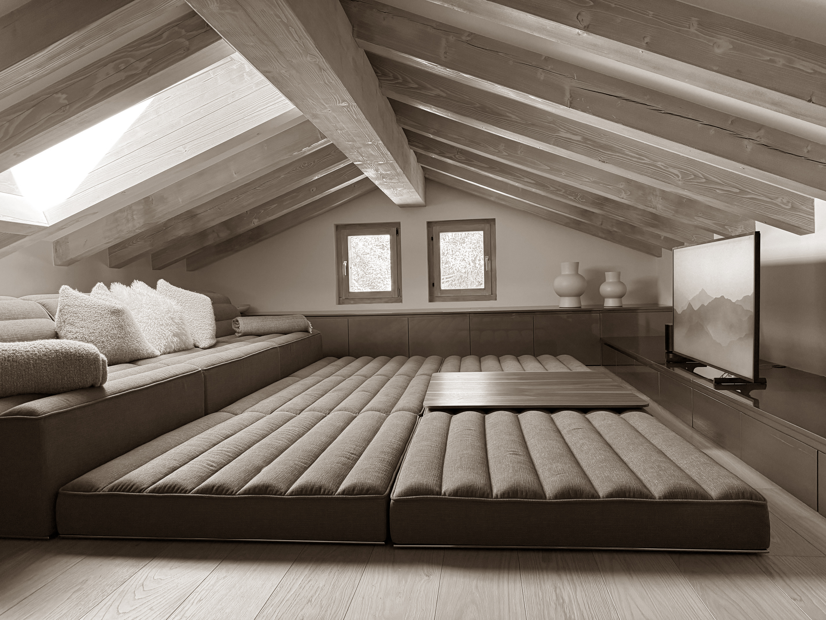 Cozy mezzanine lounge nestled under pitched wooden beams, featuring an expansive modular floor sofa with plush cushions and a central low table. Skylights and soft tones enhance the sense of calm, making it a perfect retreat for watching films or simply unwinding. Cozy mezzanine lounge nestled under pitched wooden beams, featuring an expansive modular floor sofa with plush cushions and a central low table. Skylights and soft tones enhance the sense of calm, making it a perfect retreat for watching films or simply unwinding.