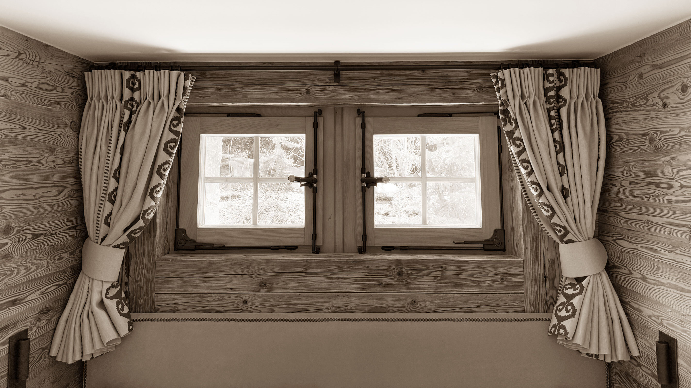 Charming wooden-framed window with traditional alpine curtains, bringing natural light and a cozy mountain feel to the space.