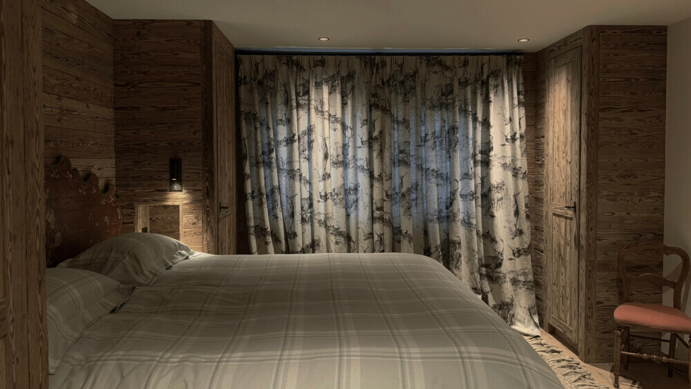 Cozy bedroom with soft lighting, wooden walls, and alpine-patterned curtains, creating a warm and restful atmosphere ideal for peaceful nights.