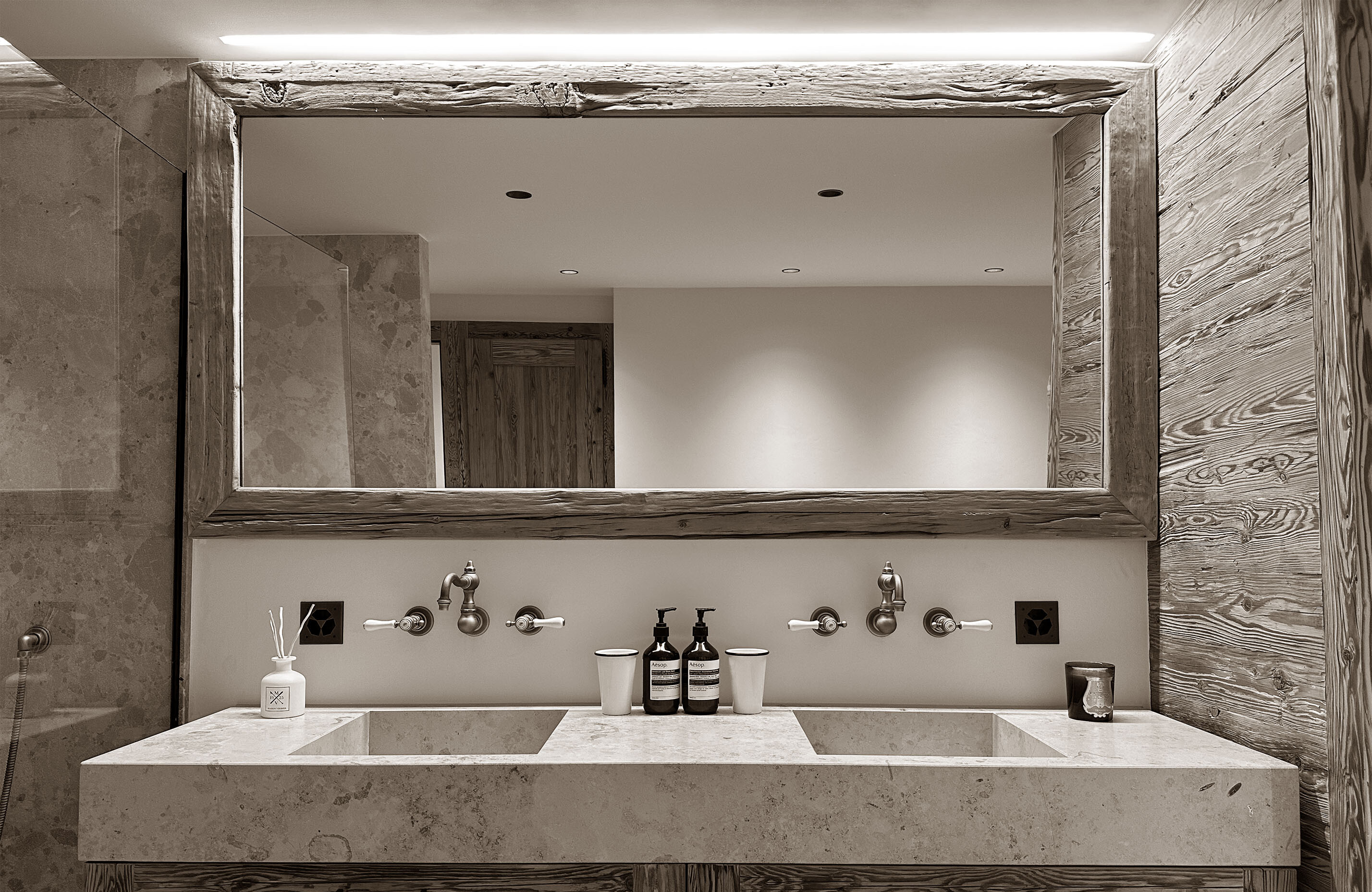 Refined bathroom with double stone sink, wide rustic mirror, and natural wood finishes, offering a clean and elegant space with a warm alpine feel.
