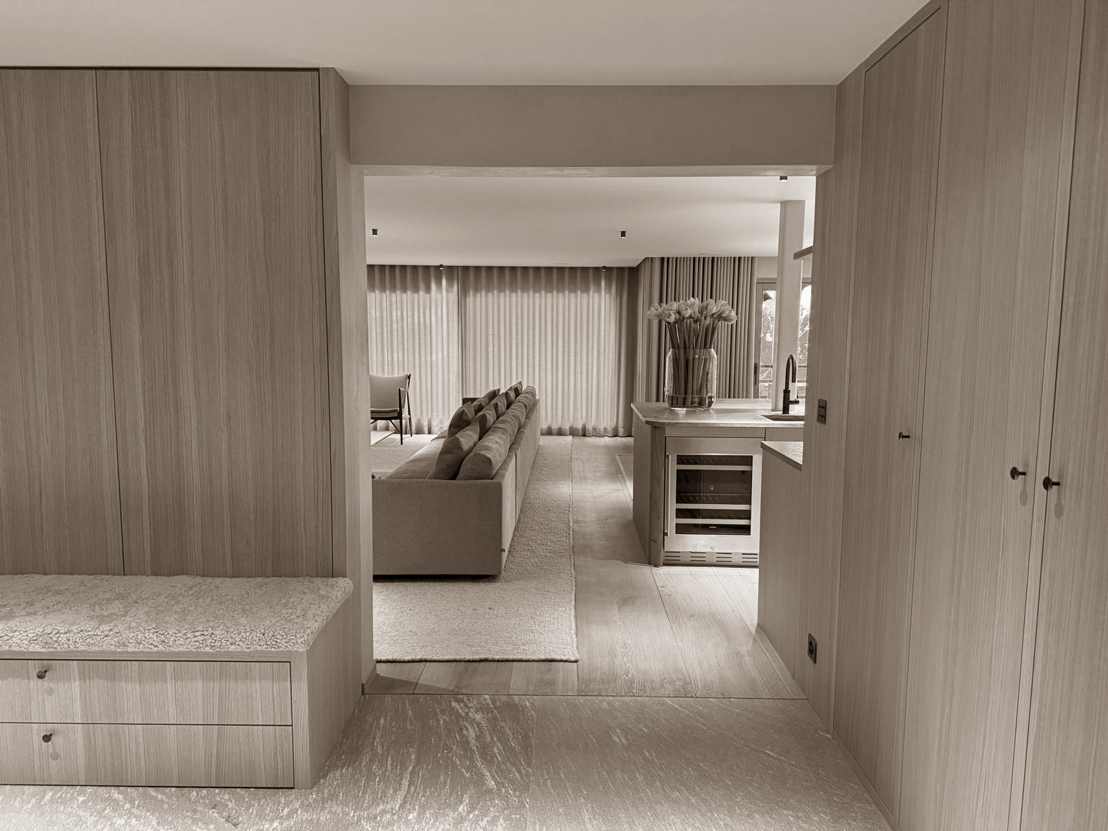 A soft transition space opens to a light-filled living area, framed by clean cabinetry and warm textures. The layout flows seamlessly from entry to kitchen to lounge, offering both elegance and ease.