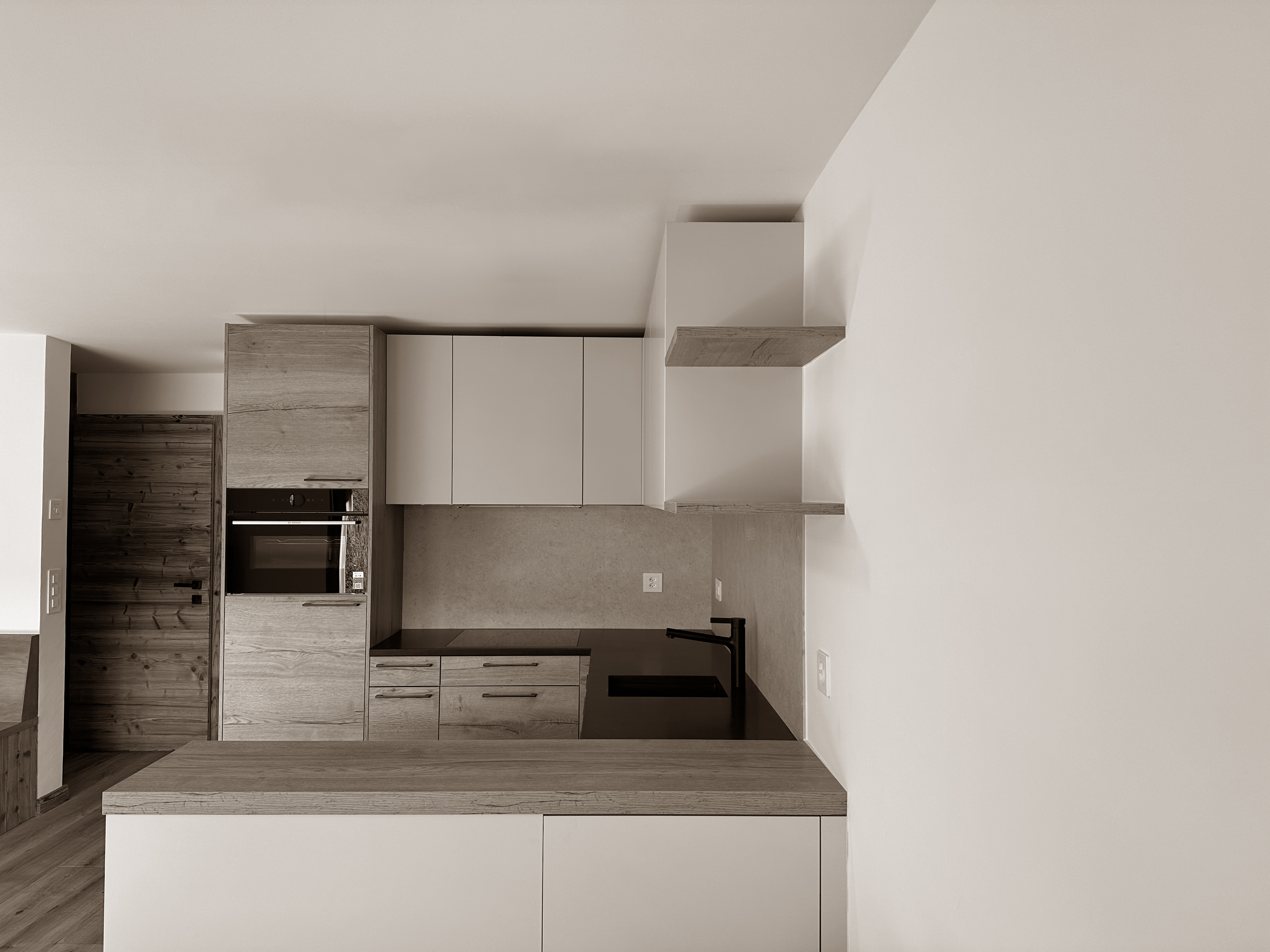 Streamlined kitchen design with soft wood finishes and minimalist white cabinetry, enhanced by open shelving and subtle textures. The compact layout is thoughtfully organized, offering both practicality and understated elegance in a cozy alpine setting.
