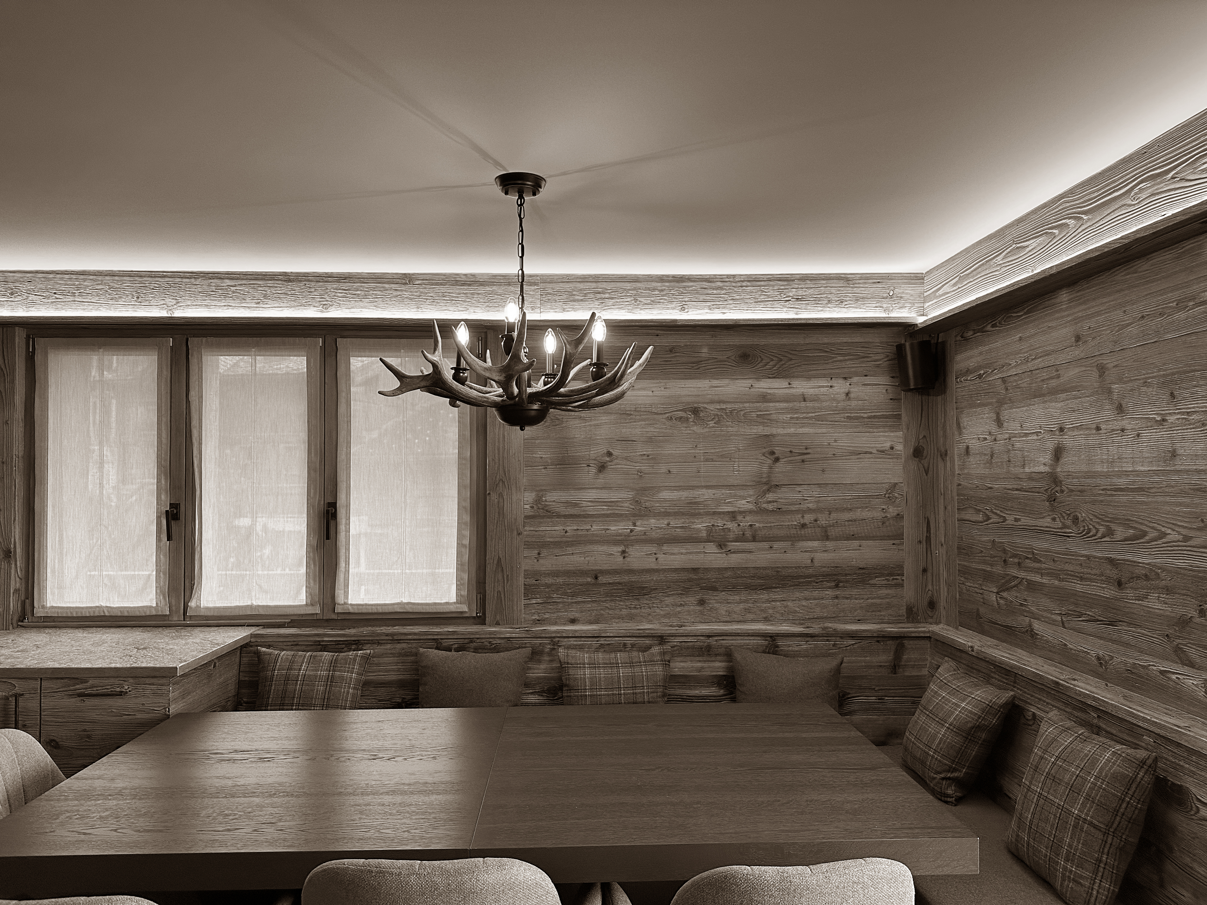 Warm and inviting dining nook clad in natural wood, featuring built-in bench seating with cozy cushions and a rustic antler-style chandelier. Soft indirect lighting and classic alpine textures create a charming, intimate space ideal for relaxed mountain gatherings.
