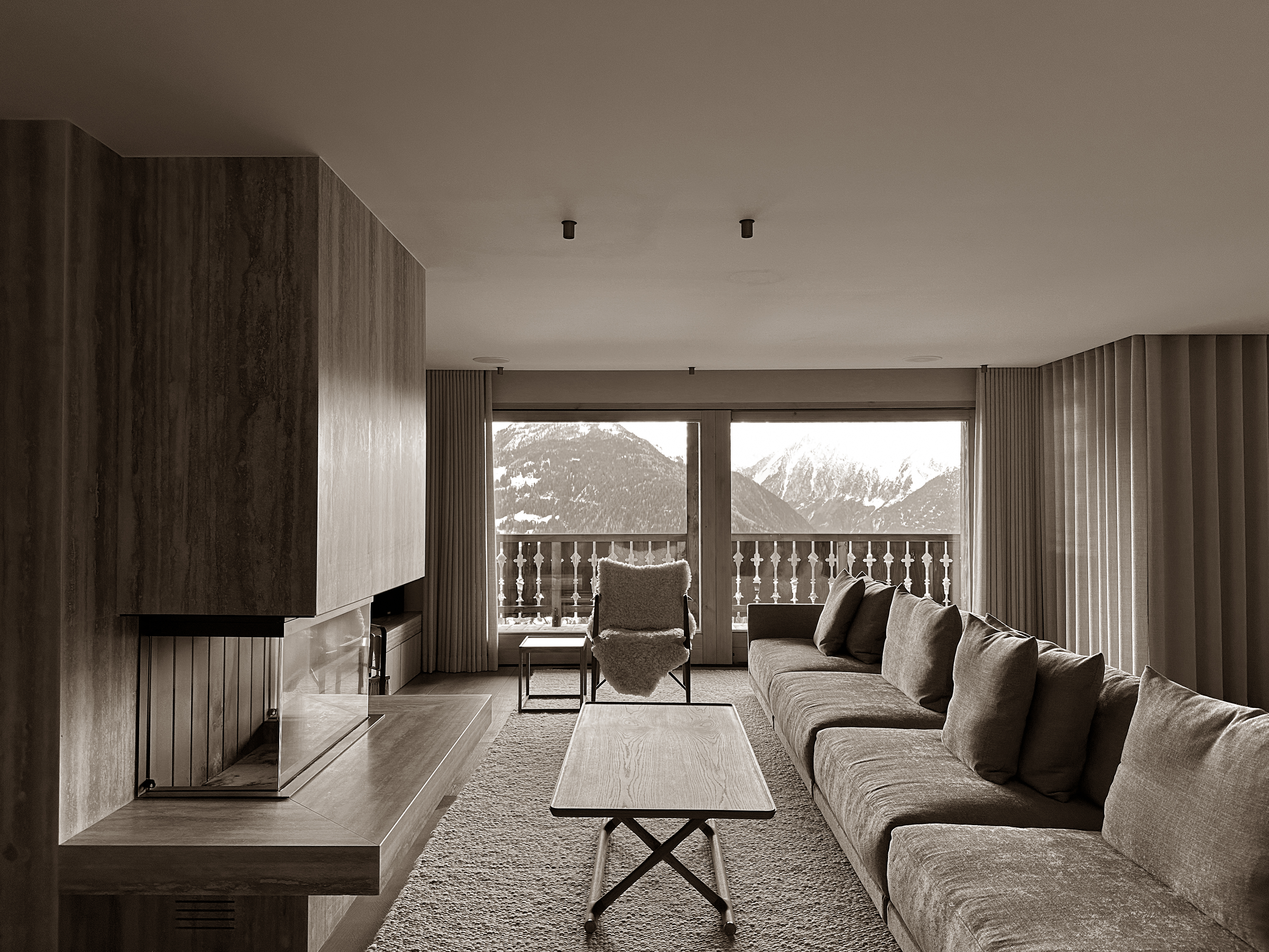 A cozy lounge with alpine views, where warm textures meet clean lines, framed by the calm of the mountains beyond.