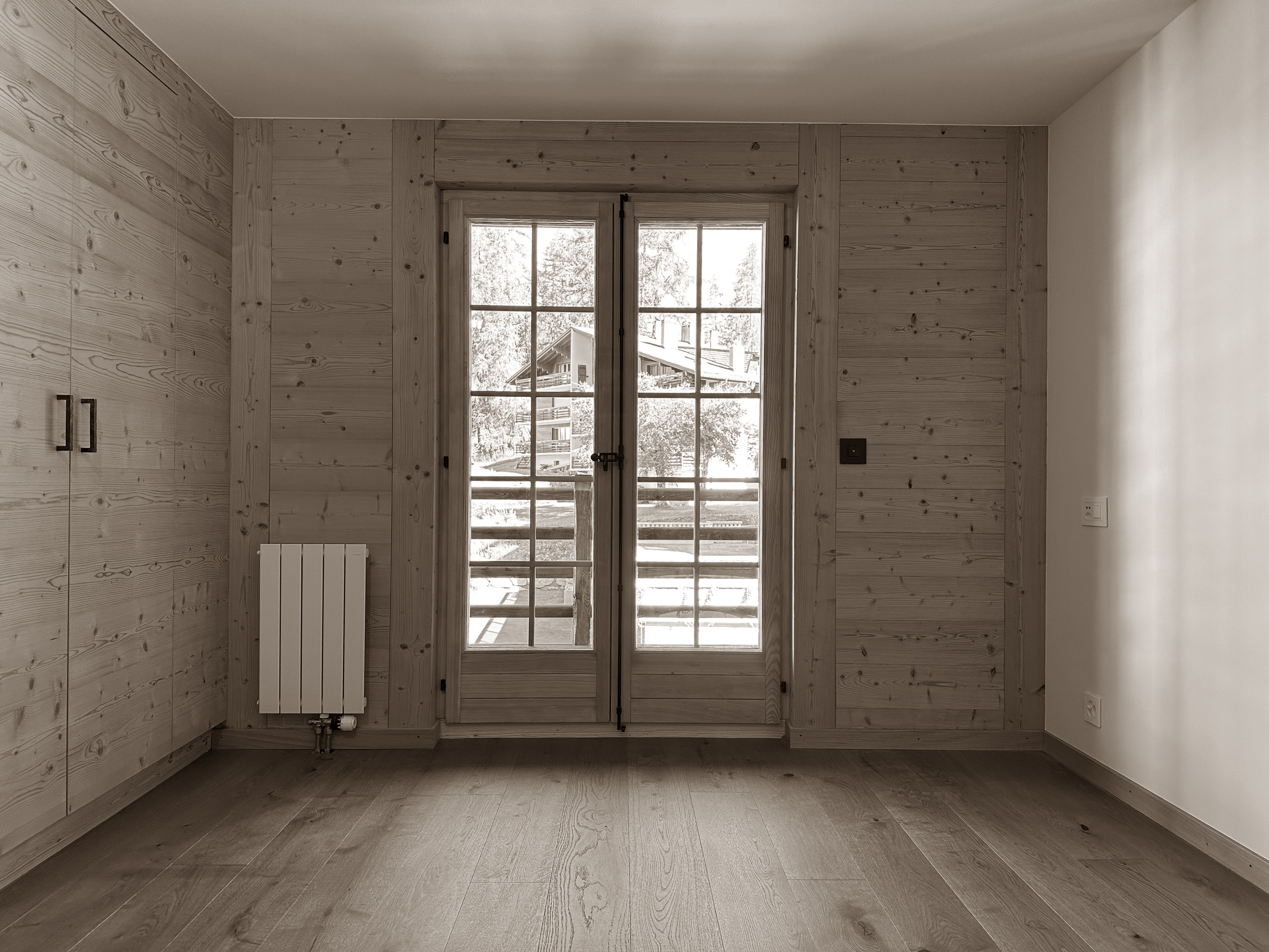 Bright bedroom space featuring natural wood paneling, built-in storage, and large doors opening onto a balcony, filling the room with natural light and offering a warm, inviting alpine ambiance.