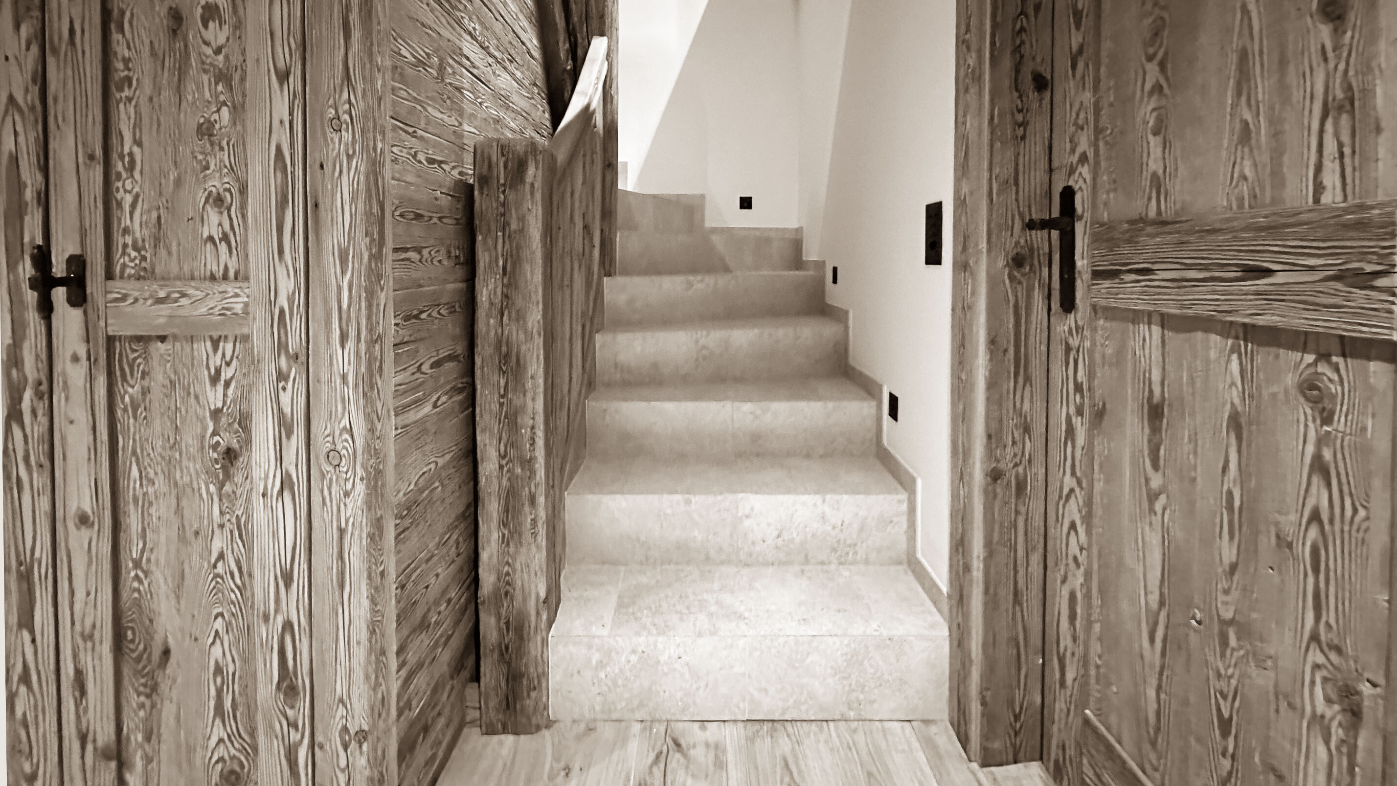Warm and simple staircase with wooden doors and natural textures, creating a cozy transition between floors in a mountain-style interior.